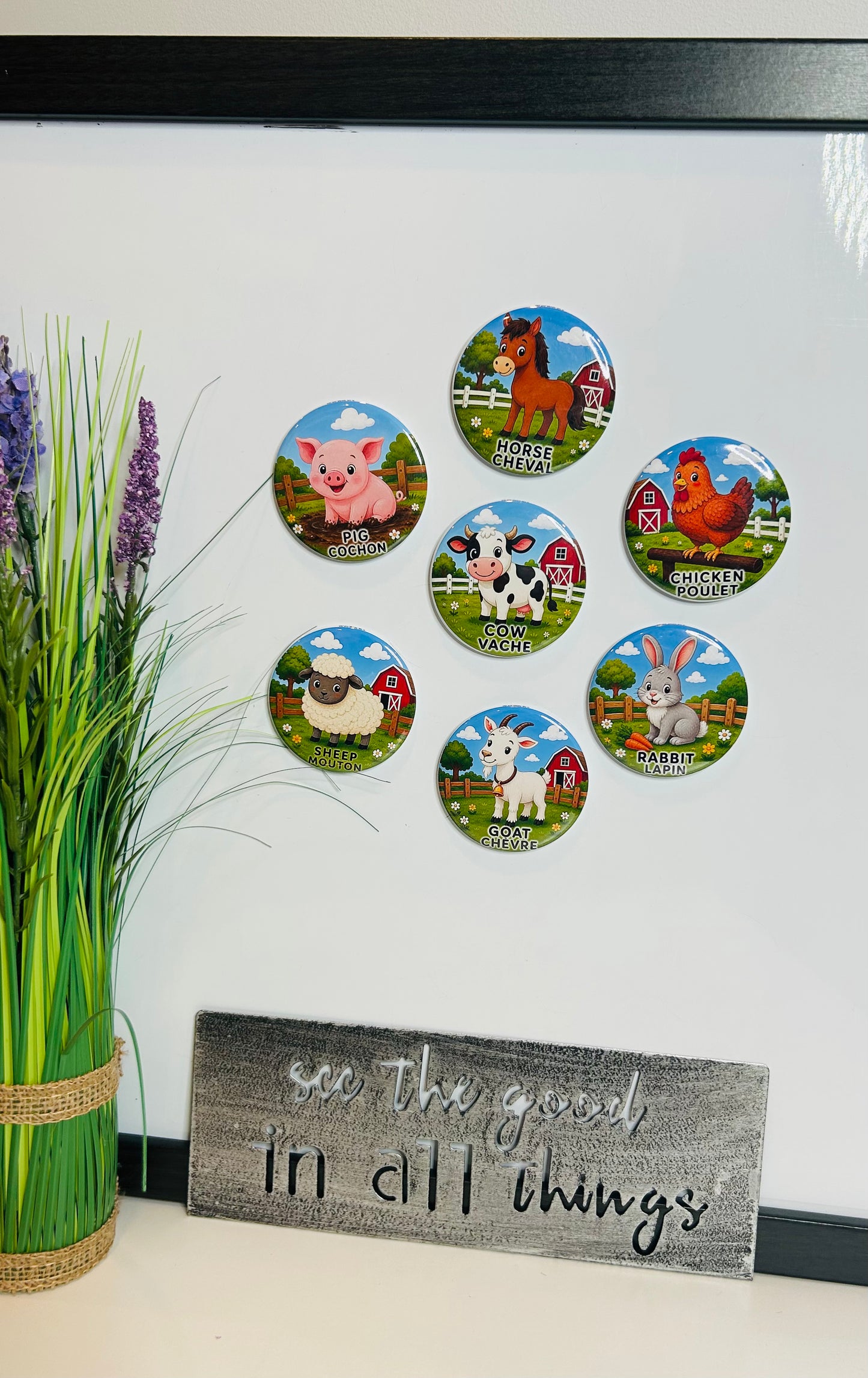 A set of seven circular farm-themed magnets displayed on a white wall above a rustic wooden sign that reads 'see the good in all things'. The magnets feature colorful illustrations of a pig, horse, cow, chicken, sheep, goat, and rooster in green fields.